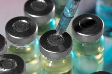 Filling syringe with medicine from vial on light background, closeup