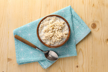 Tasty boiled oatmeal in bowl and spoon on wooden table, top view