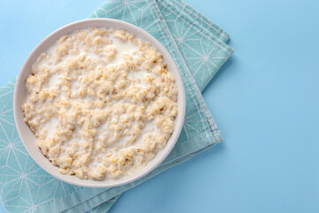Tasty boiled oatmeal in bowl on light blue table, top view. Space for text