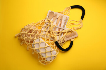 Fishnet bag with different items on yellow background, top view. Conscious consumption