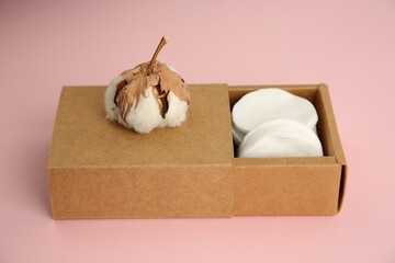 Cardboard box with cotton pads and flower on pink background, closeup