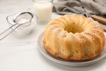 Delicious sponge cake with powdered sugar and glass of milk on white table, closeup