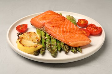 Tasty grilled salmon with asparagus, tomatoes, spices and lemon on light grey table