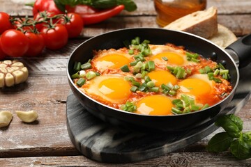 Delicious Shakshuka in frying pan on wooden table, closeup