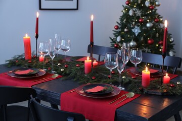Elegant Christmas table setting with dishware and burning candles in festively decorated room