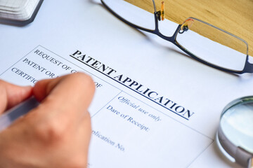 Woman filling out Patent Application form to publish invention. Close-up view, selective focus.