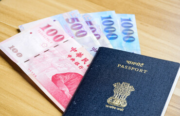 New Taiwan dollar bank notes and Indian passport on wooden desk. Travel work abroad labor agreement concept.