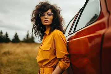  woman in orange dress and glasses standing in the field against a yellow vintage car. © hisilly