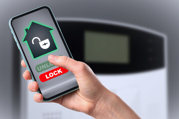 Woman operating home alarm system via mobile phone against grey wall with security control panel, closeup. Application interface on device screen