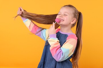 Happy little girl with lollipop on orange background