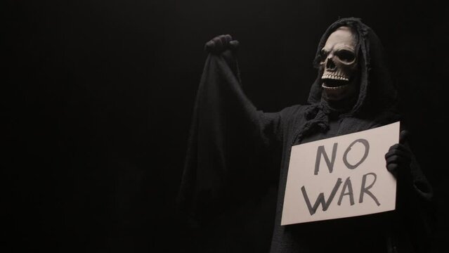 A man dressed as a grim reaper agitates people with a No War sign in his hands. There is darkness in the background. Costume for Halloween. Halloween characters concept.