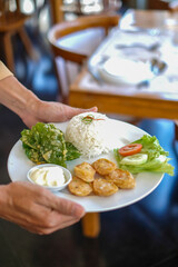 waiters in Indonesia carry white plates containing the food that will be served. the food consists of vegetables, meat and mayonnaise