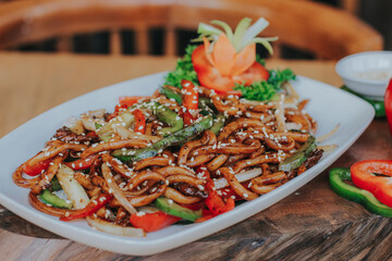 fried udon seafood with vegetables. served in white plate with hand and table of the restaurant