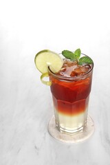 A clear glass containing ice lemon tea with garnish of lemon slices and mint leaves