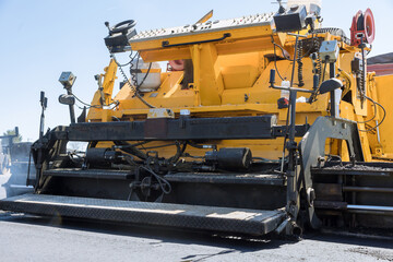 During highway construction, pavement machine lays fresh bitumen asphalt over gravel base
