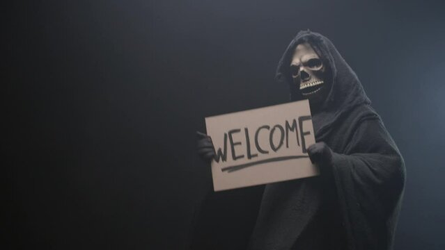 Grim reaper holding a Welcome sign and luring people to him, dancing, on the black background. Mysticism and the afterlife.