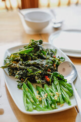 fried cooked green vegetables called kailan served on a restaurant dining table using a white plate