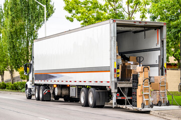 Carts with cargo delivered by the day cab big rig semi truck stand on the lift platform at the rear...