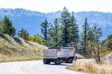 Heavy duty big rig tipper semi truck with two tip trailers running on the mountain winding road...