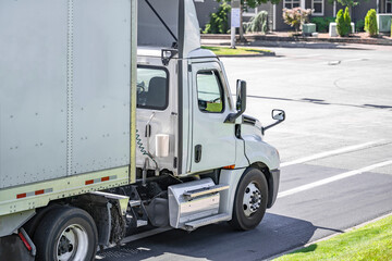 Local carrier day cab big rig semi truck with dry van semi trailer running on the city street for...