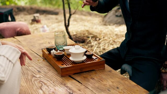 close-up The hands of a professional tea master who pours fresh natural green tea from a glass teapot into bowls on wooden chaban table