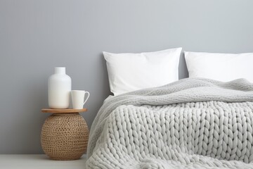Fototapeta na wymiar Cozy stylish Scandinavian room with a grey stucco wall featuring a white and grey knitted woolen blanket laid on a white bedside table