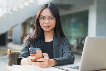 Young confident businesswoman using her smart phone while sitting at the office desk.