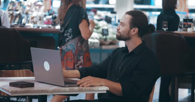 Young bearded guy in a black shirt, website developer sitting in a cafe and typing on laptop, drinking coffe. Specialization website developer. Creating design of website for business or personal use.