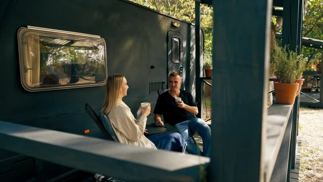 A young handsome guy and a girl are sitting on the veranda of a mobile home in camper drinking tea and talking enthusiastically