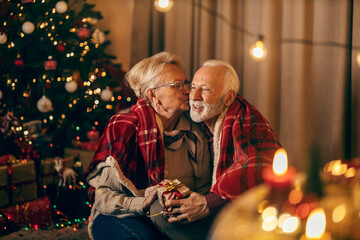 A senior couple celebrating New Year and christmas at home while sharing gifts and kissing.