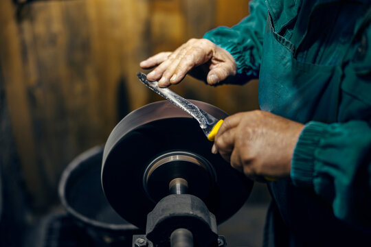 Cropped picture of craftsman's hands sharpening knife in his workshop.