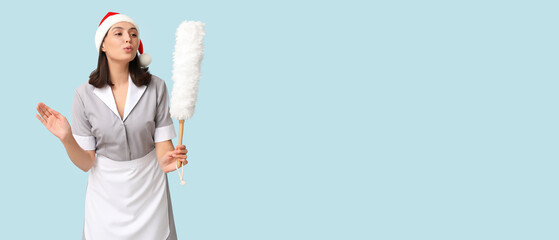 Beautiful female chambermaid in Santa hat on light blue background with space for text