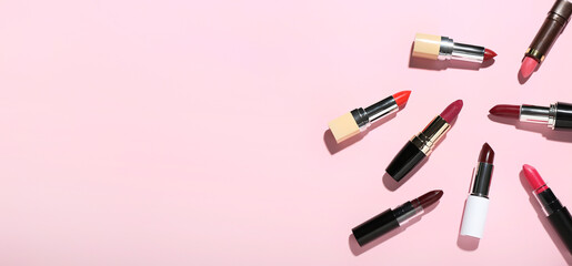 Many different lipsticks on pink background with space for text