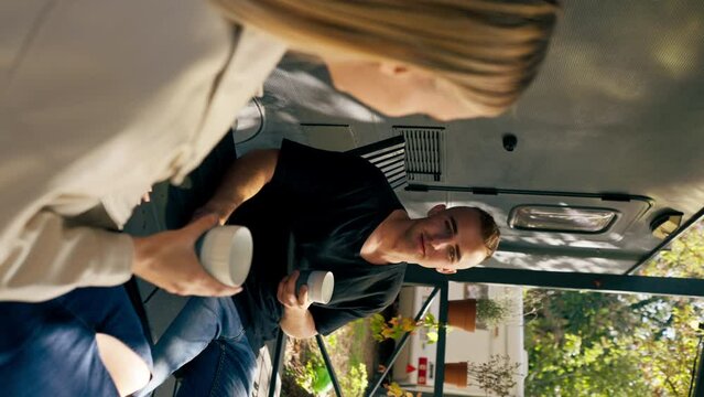 vertical video A young handsome guy and a girl are sitting on the veranda of a mobile home in camper drinking tea and talking enthusiastically