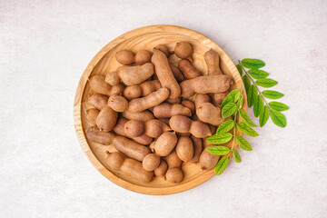 Plate of tasty tamarinds and leaves on white background