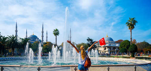 Happy woman tourist with turkish flag enjoys Istanbul city- Blue mosque, Hagia Sophia mosque, fountain and palm tree in Turkey - obrazy, fototapety, plakaty