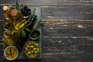 Bowls and glassware with fresh olive oil on black wooden background