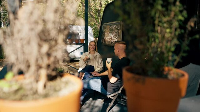 A young handsome guy and a girl are sitting on the veranda of a mobile home in camper drinking tea and talking enthusiastically