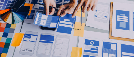 Close up ux developer and ui designer brainstorming about mobile app interface wireframe design on table with customer breif and color code at modern office.Creative digital development agency