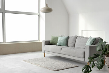 Interior of light living room with grey sofa, Monstera plant and lamp