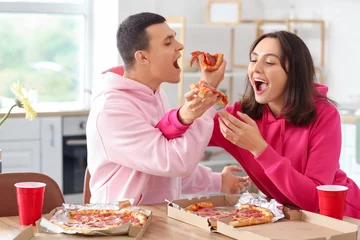 Fotobehang Young couple eating tasty pepperoni pizza in kitchen © Pixel-Shot
