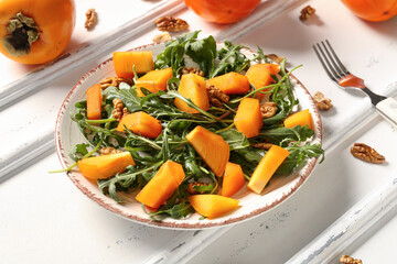 Plate of delicious salad with persimmon and walnut on white background