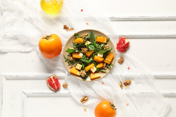Plate of delicious salad with persimmon, walnut and pomegranate seeds on white background