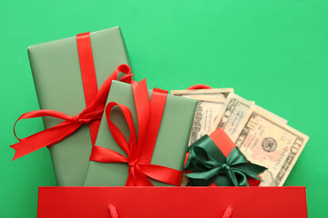 Shopping bag with Christmas gift boxes and money on green background