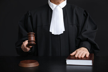 Female judge with gavel and book at table on black background