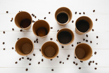 Cups of hot coffee and beans on white wooden background