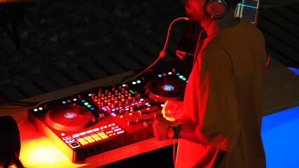 DJ wearing headphones stands at music console in nightclub.