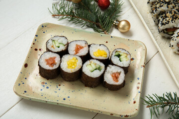 Plate of tasty sushi rolls with fir branches and Christmas balls on white wooden background