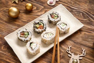 Plate with tasty sushi rolls and Christmas decorations on wooden background