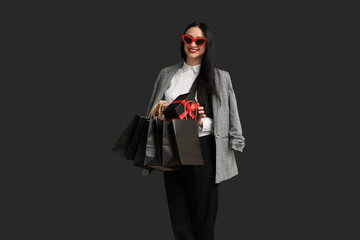 Beautiful stylish woman with shopping bags and gift box on dark background. Black Friday Sale